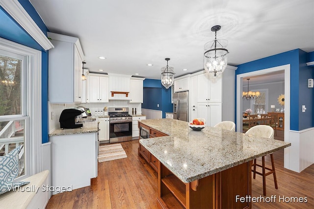 kitchen with appliances with stainless steel finishes, dark wood-type flooring, a center island, a notable chandelier, and a sink