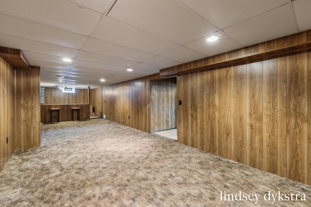 finished below grade area with a paneled ceiling, wooden walls, carpet flooring, and recessed lighting