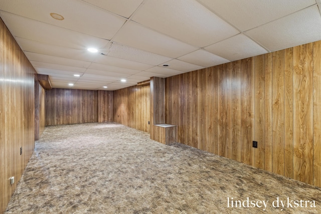 finished basement featuring wooden walls, a drop ceiling, and carpet flooring