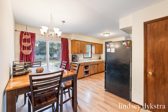 kitchen featuring brown cabinets, light countertops, light wood-style flooring, freestanding refrigerator, and a chandelier