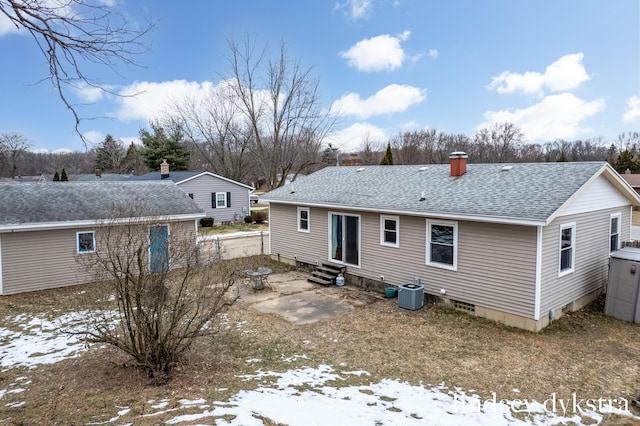 rear view of property with entry steps, a shingled roof, a chimney, and central AC