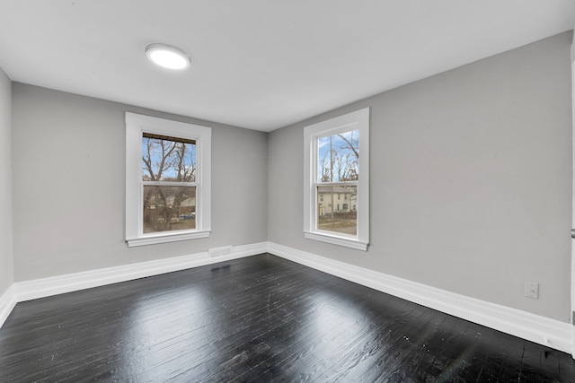 empty room with dark wood-style floors, visible vents, and baseboards