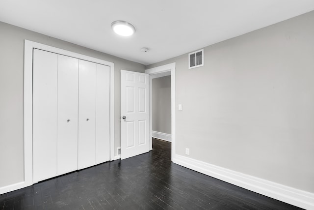 unfurnished bedroom with a closet, dark wood-style flooring, visible vents, and baseboards