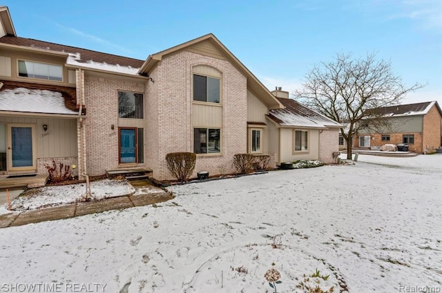 snow covered property with a chimney and brick siding