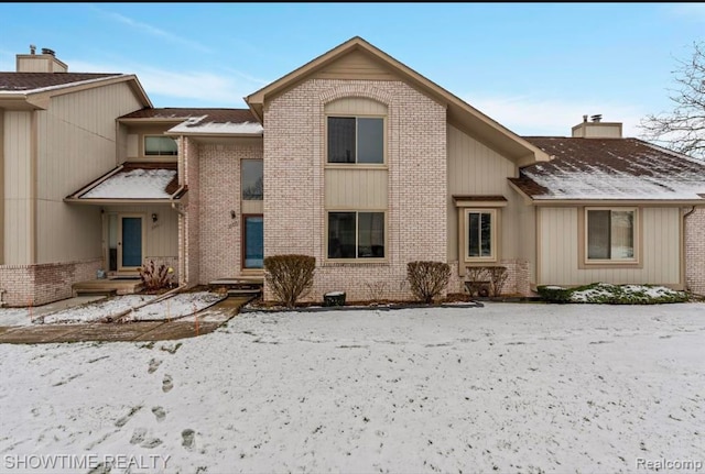 snow covered property featuring a chimney and brick siding