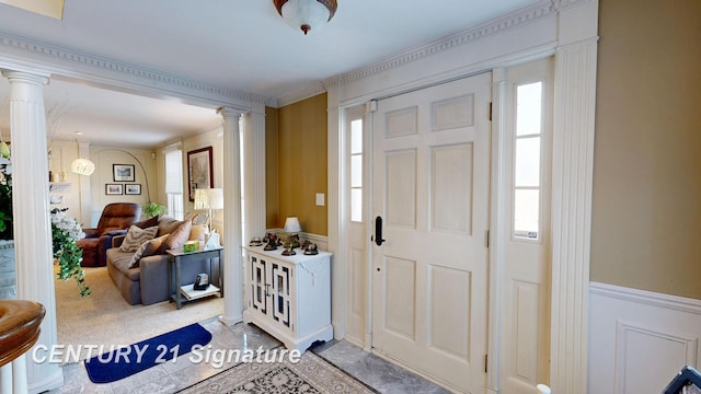 entryway featuring a healthy amount of sunlight, ornate columns, a decorative wall, and a wainscoted wall