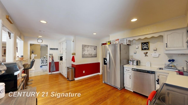 kitchen with stainless steel appliances, light countertops, a sink, and light wood finished floors