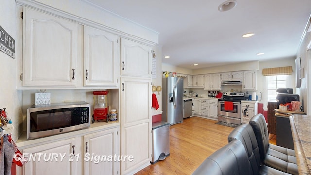 kitchen featuring light wood finished floors, stainless steel appliances, light countertops, white cabinetry, and under cabinet range hood