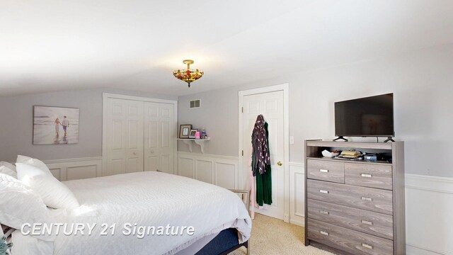 bedroom with light colored carpet, a wainscoted wall, visible vents, and vaulted ceiling