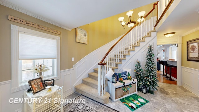 staircase featuring a chandelier, wainscoting, a decorative wall, and crown molding