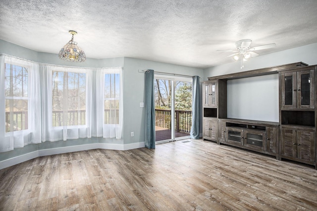 unfurnished living room with a ceiling fan, a textured ceiling, baseboards, and wood finished floors