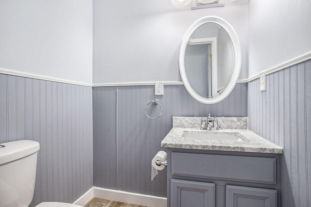 bathroom with a wainscoted wall, vanity, and toilet