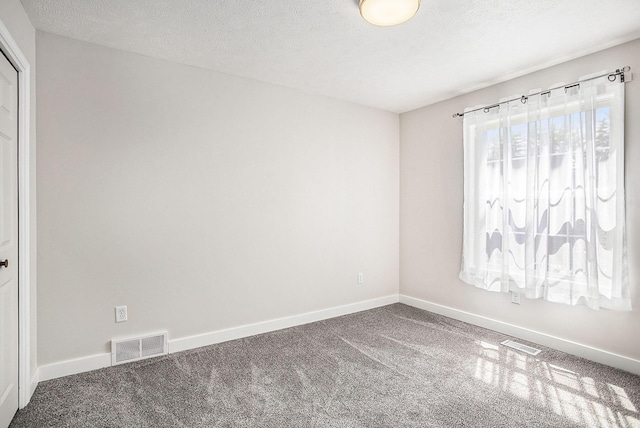 unfurnished room with a textured ceiling, carpet flooring, visible vents, and baseboards