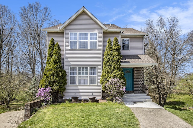 traditional home featuring a front lawn, roof with shingles, and brick siding