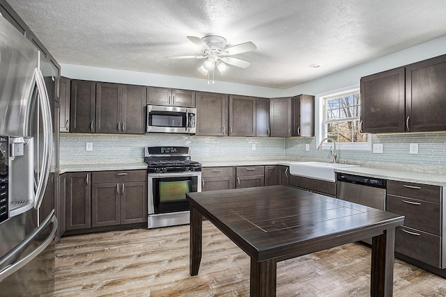 kitchen with stainless steel appliances, dark brown cabinets, light wood-type flooring, and a sink