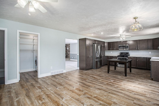 kitchen with light wood finished floors, stainless steel appliances, tasteful backsplash, visible vents, and dark brown cabinetry