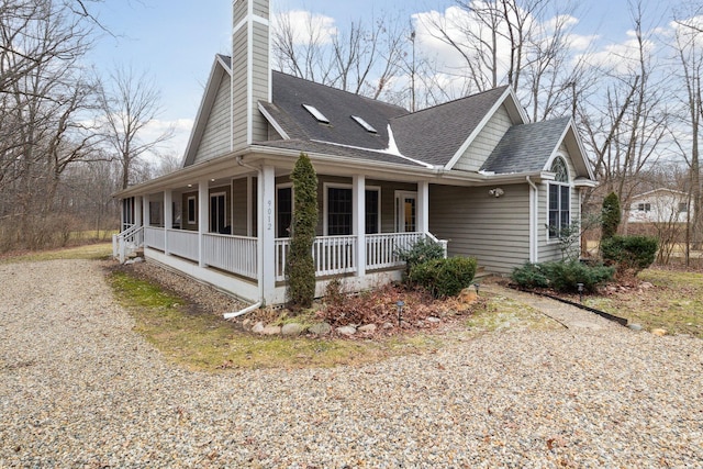 view of front of home featuring driveway, a porch, a chimney, and a shingled roof