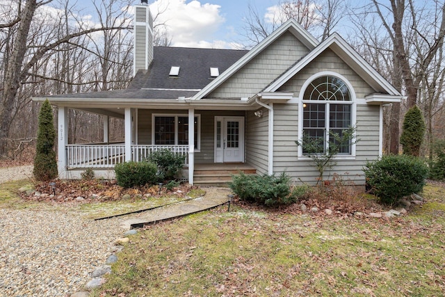 view of front facade featuring roof with shingles, a porch, and a chimney