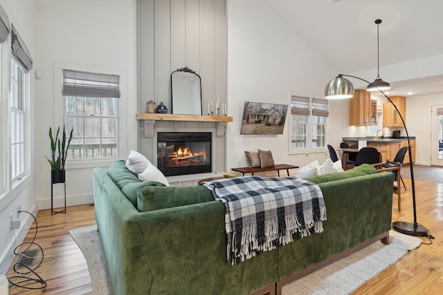 living room featuring a large fireplace, high vaulted ceiling, wood finished floors, and baseboards