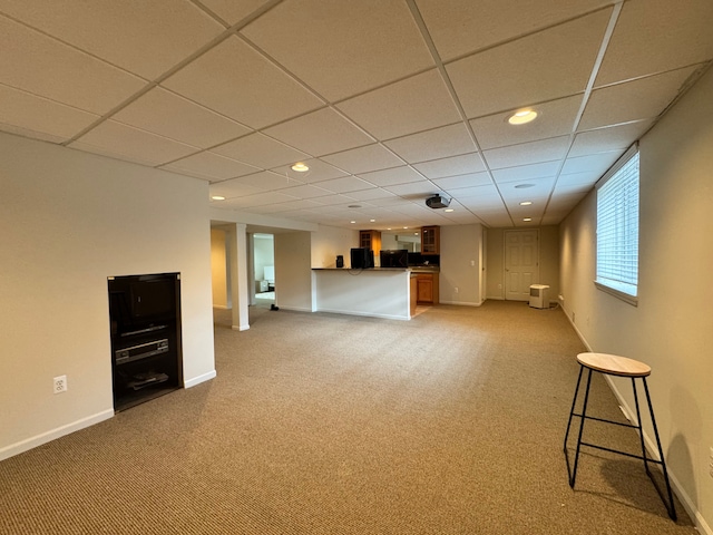 unfurnished living room with a paneled ceiling, baseboards, light carpet, and bar area