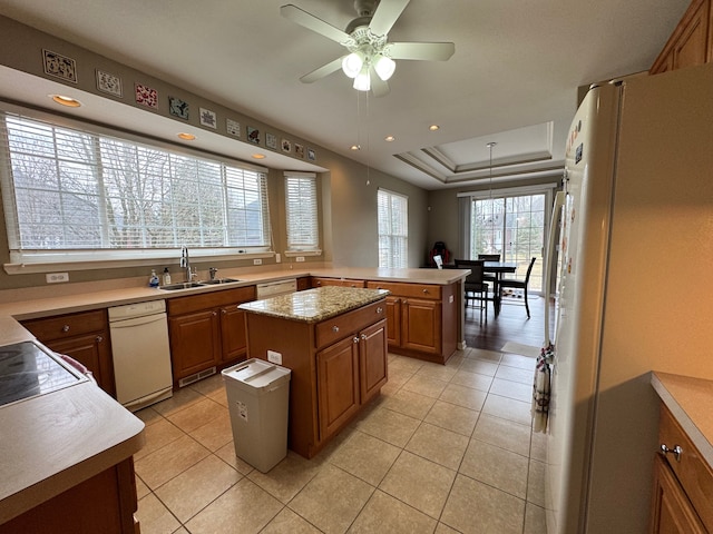kitchen with white appliances, a ceiling fan, brown cabinetry, a sink, and a raised ceiling