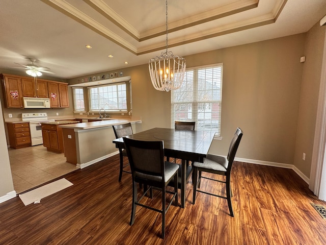 dining room featuring ornamental molding, ceiling fan with notable chandelier, a tray ceiling, dark wood-style floors, and baseboards