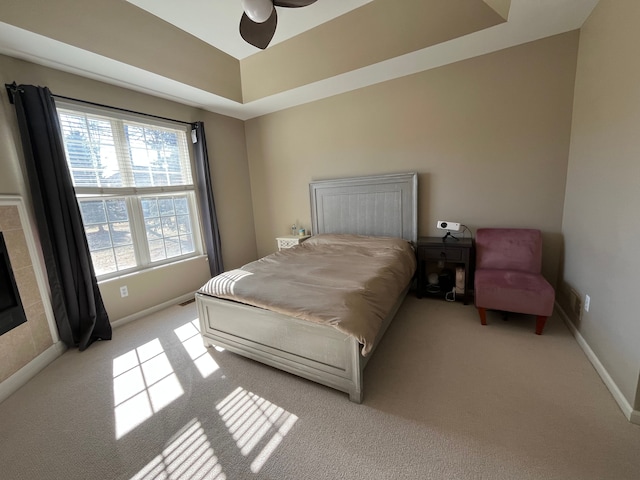 bedroom featuring baseboards, a raised ceiling, light carpet, and ceiling fan