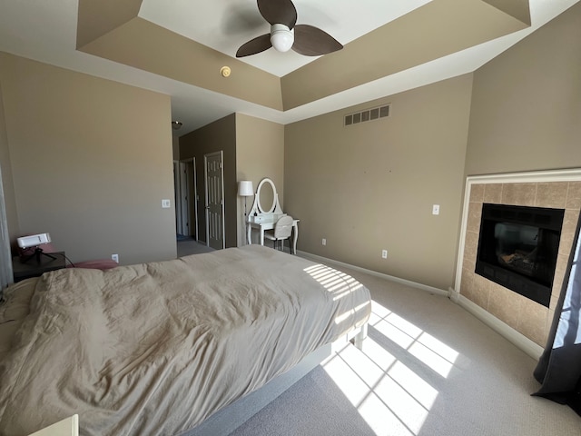 carpeted bedroom with visible vents, baseboards, a tray ceiling, a fireplace, and ceiling fan