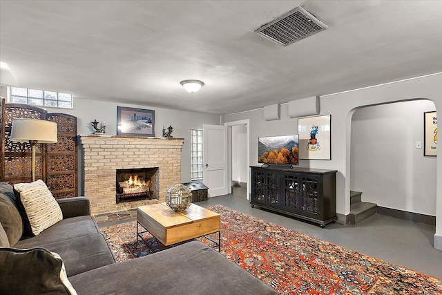 living room with visible vents, baseboards, finished concrete floors, a fireplace, and arched walkways