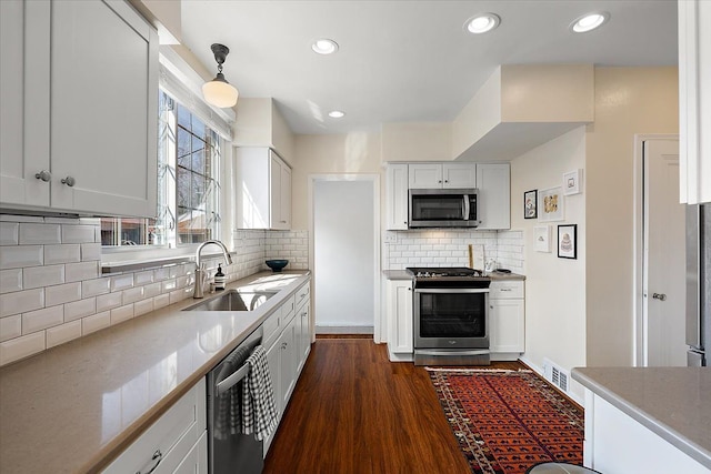 kitchen featuring dark wood finished floors, a sink, appliances with stainless steel finishes, white cabinetry, and backsplash