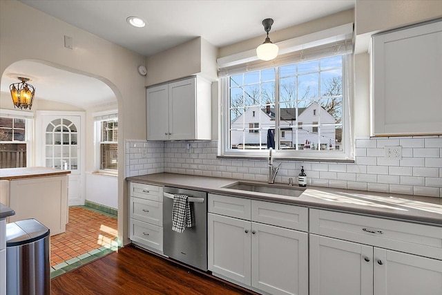 kitchen with dark wood finished floors, decorative backsplash, stainless steel dishwasher, arched walkways, and a sink