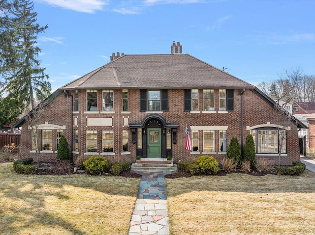 view of front of home with brick siding, a chimney, a front lawn, and fence