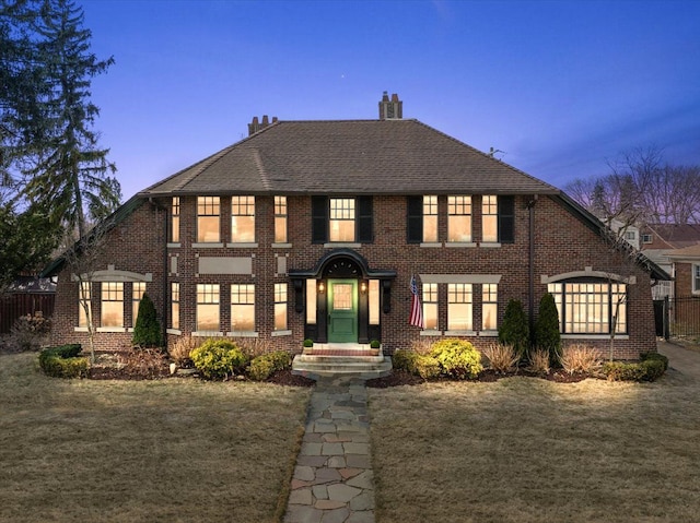 colonial inspired home featuring brick siding, a lawn, fence, and a chimney