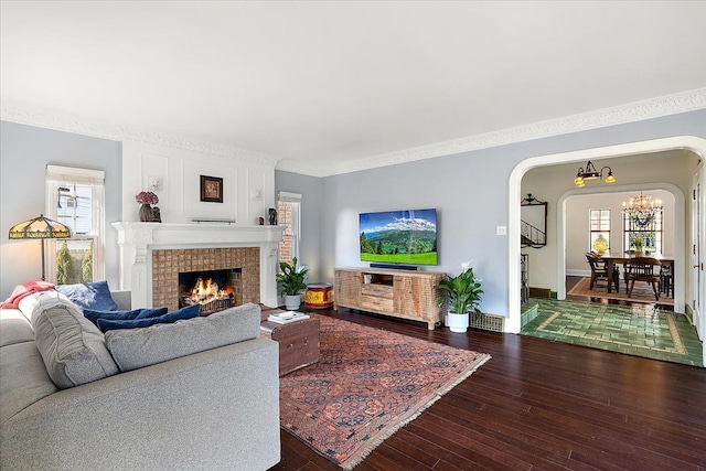 living area with hardwood / wood-style flooring, arched walkways, crown molding, a fireplace, and baseboards