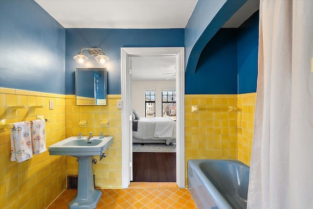 full bathroom with tile patterned floors, a bath, tile walls, and a wainscoted wall