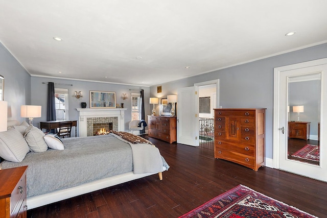 bedroom featuring dark wood-type flooring, baseboards, crown molding, recessed lighting, and a warm lit fireplace