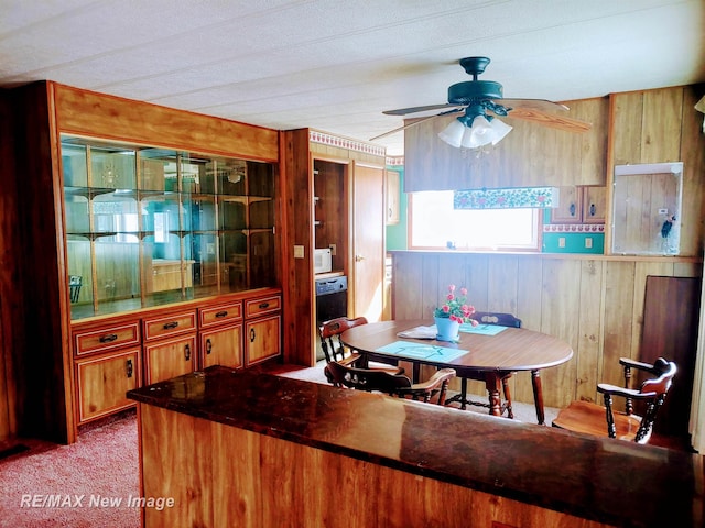 carpeted dining room with ceiling fan and wooden walls