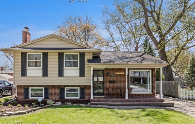 tri-level home with brick siding, a chimney, a front yard, and fence