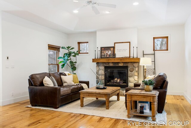 living room featuring baseboards, a stone fireplace, a tray ceiling, and light wood-style floors