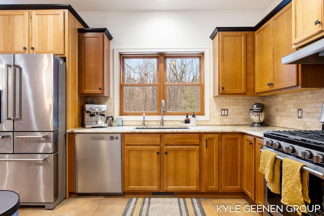 kitchen featuring decorative backsplash, light stone counters, stainless steel appliances, under cabinet range hood, and a sink