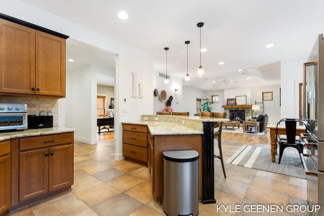 kitchen with a breakfast bar, brown cabinets, recessed lighting, ceiling fan, and a stone fireplace