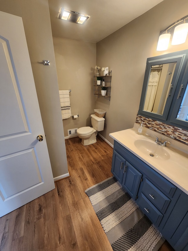 bathroom featuring visible vents, toilet, decorative backsplash, vanity, and wood finished floors