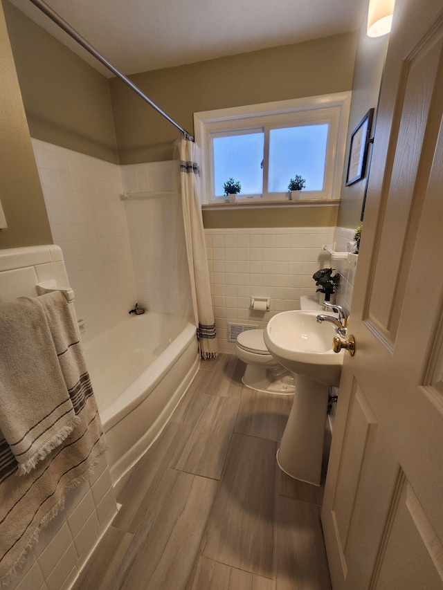 bathroom featuring toilet, a wainscoted wall, visible vents, tile walls, and shower / bathtub combination with curtain