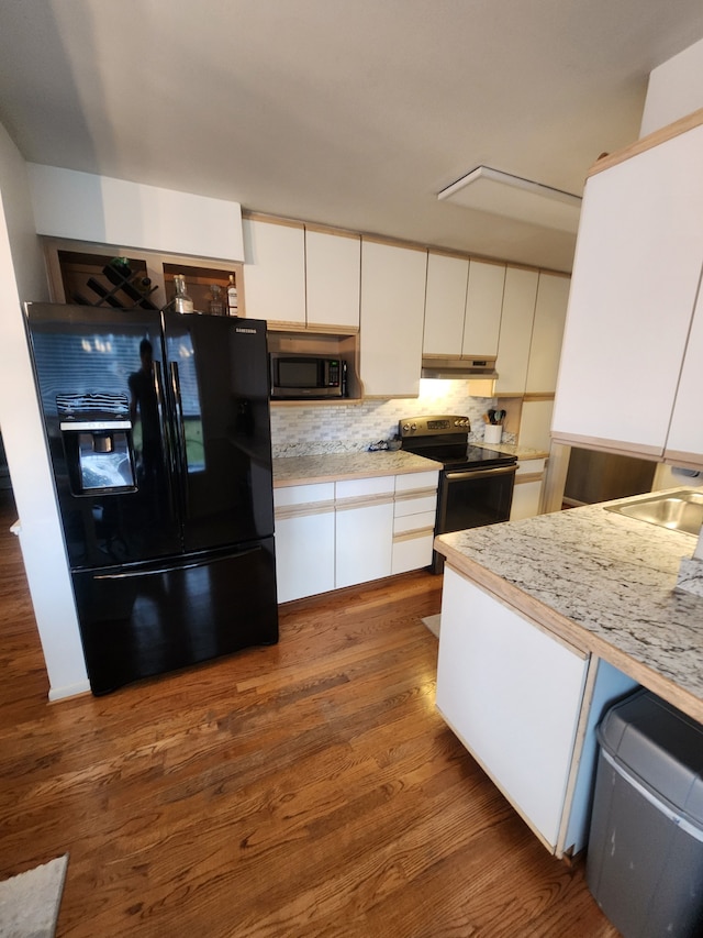 kitchen featuring under cabinet range hood, range with electric stovetop, light countertops, black refrigerator with ice dispenser, and stainless steel microwave