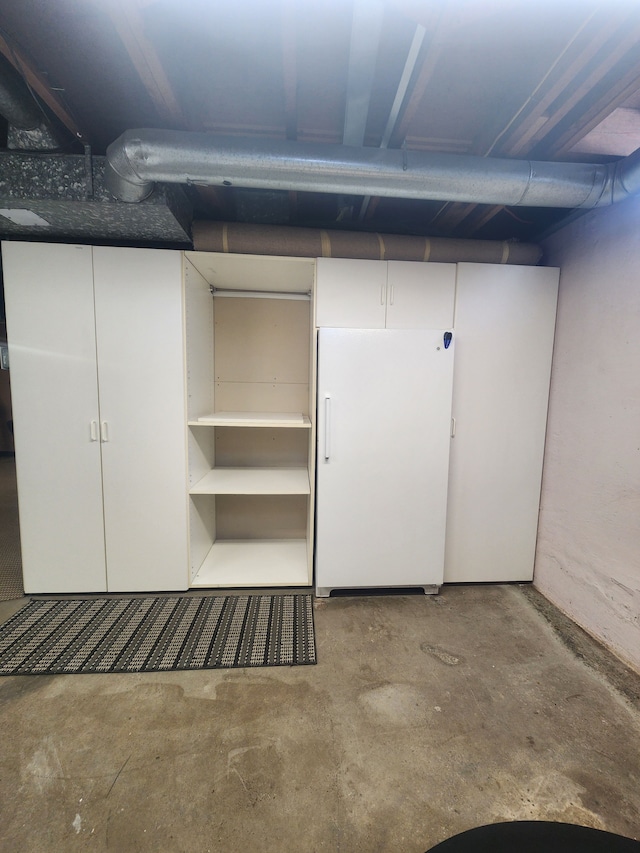 unfinished basement featuring freestanding refrigerator