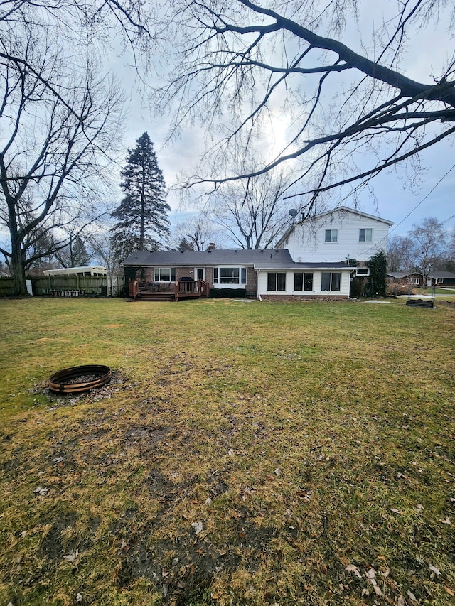 view of front facade featuring a deck, fence, a fire pit, and a front lawn