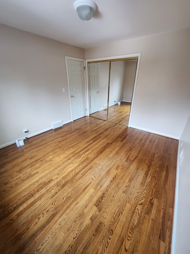 unfurnished bedroom featuring a closet, wood finished floors, visible vents, and baseboards