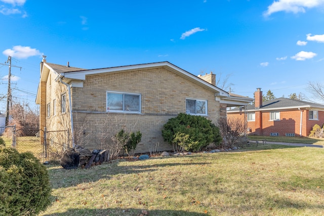 view of side of property featuring a yard, brick siding, a chimney, and fence