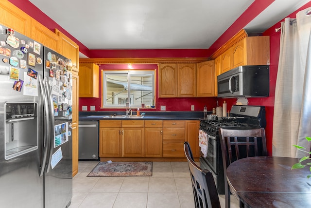 kitchen with light tile patterned floors, stainless steel appliances, dark countertops, brown cabinetry, and a sink