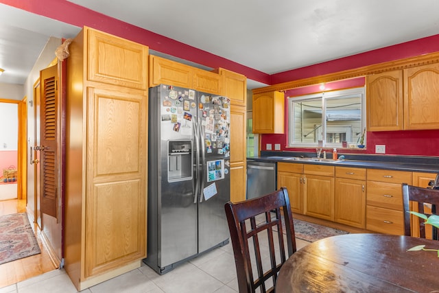 kitchen with dark countertops, light tile patterned floors, stainless steel appliances, and a sink